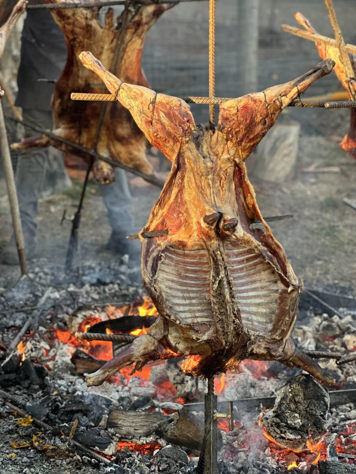 Whole lamb, cordero a la cruz, roasting on a metal cross over an open wood fire